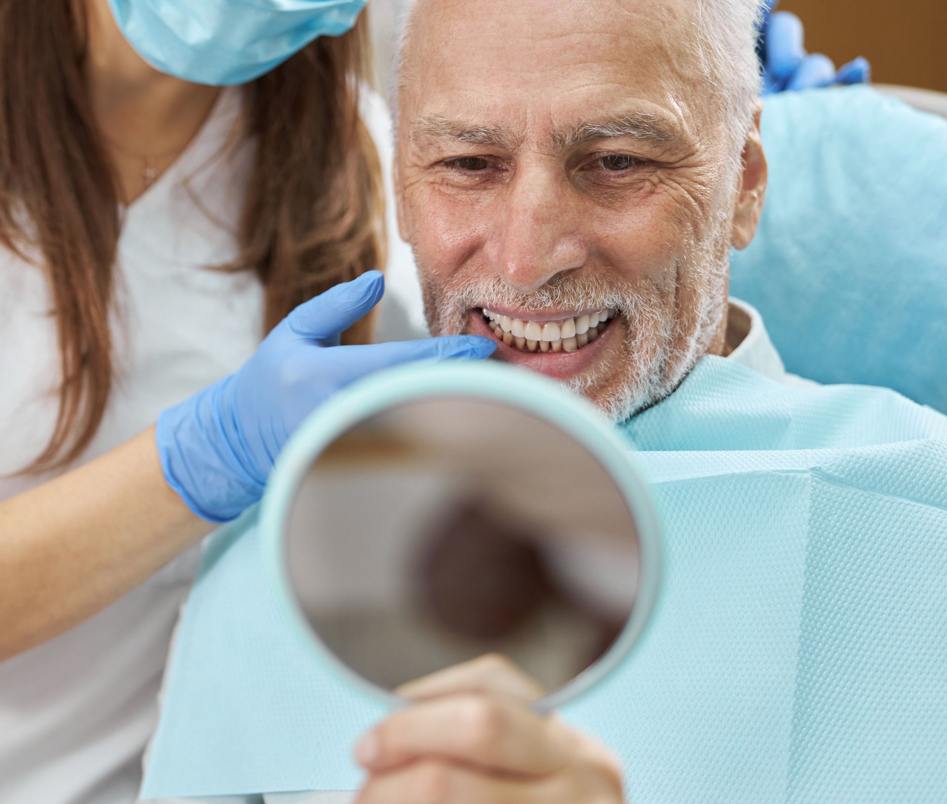 Uomo adulto sorridere felice e guarda allo specchio le sue arcate dentarie riabilitate grazie agli impianti dentali eseguiti da Dentisti Pagnoni di Ascoli Piceno